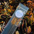 hand made incense sticks with the scent of comforting sandalwood and rose are laid out on a bed of succulent flowers in warm sunlight
