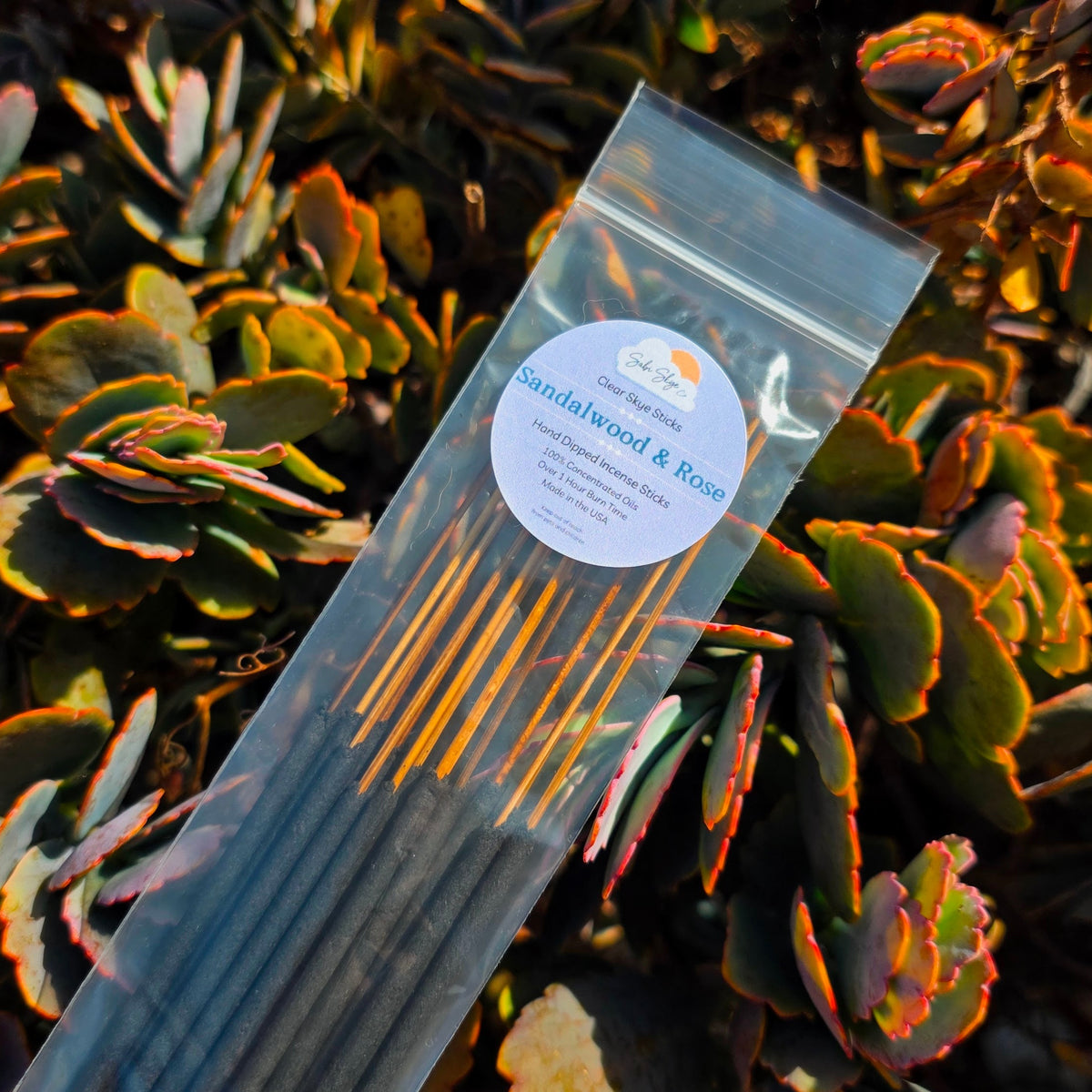 hand made incense sticks with the scent of comforting sandalwood and rose are laid out on a bed of succulent flowers in warm sunlight